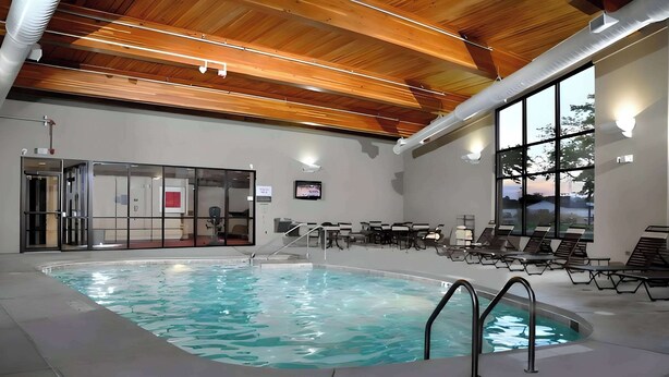 Una piscina interior con techo de madera, sillones de descanso y una pantalla de televisión.