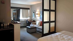 Una habitación de hotel con cama, escritorio con computadora, sofá y un ventanal con cortinas.