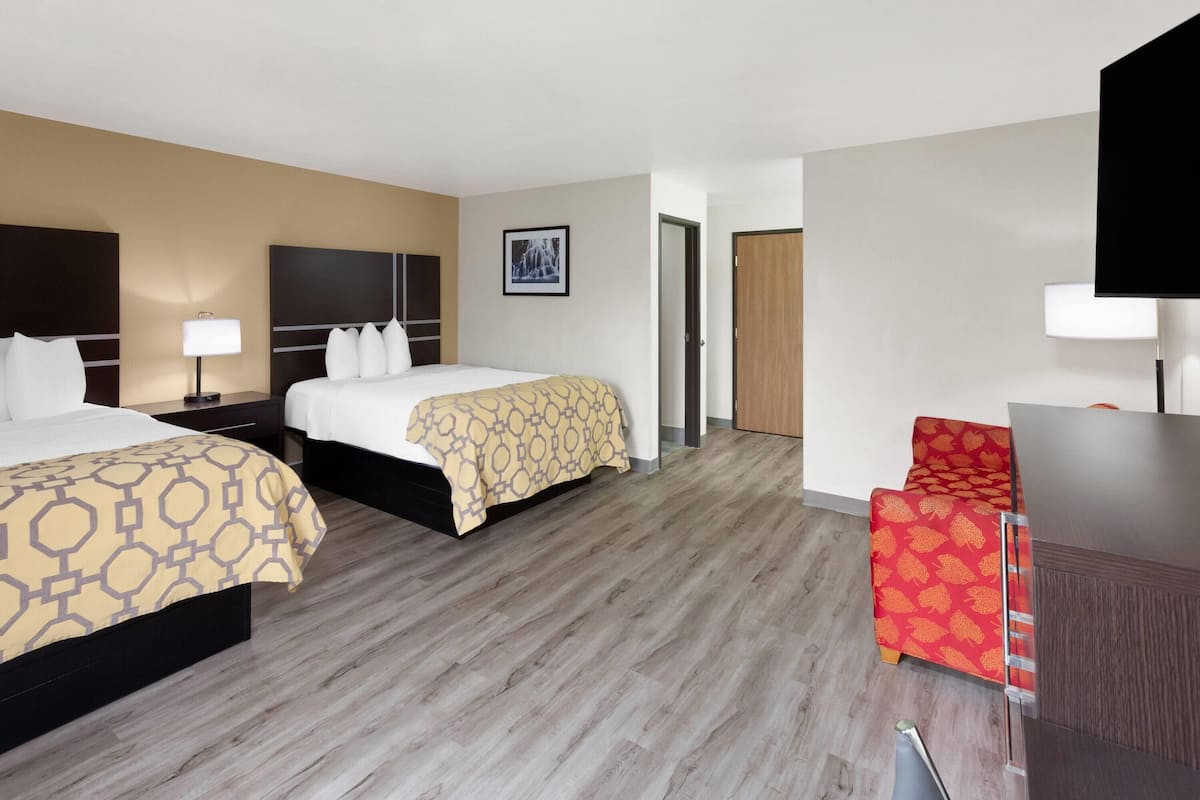 A hotel room with two beds, a desk, a chair, and a television.