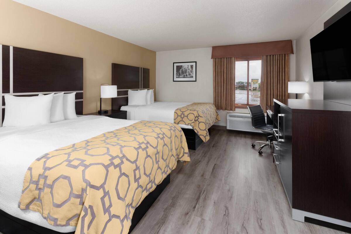 A hotel room with two beds, a desk, a chair, a TV, and a window with curtains.