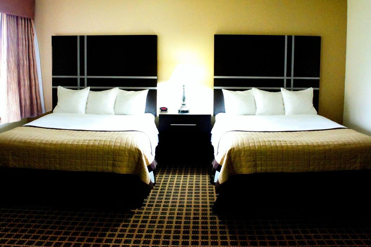 A hotel room with two beds, a nightstand, and a lamp between them.
