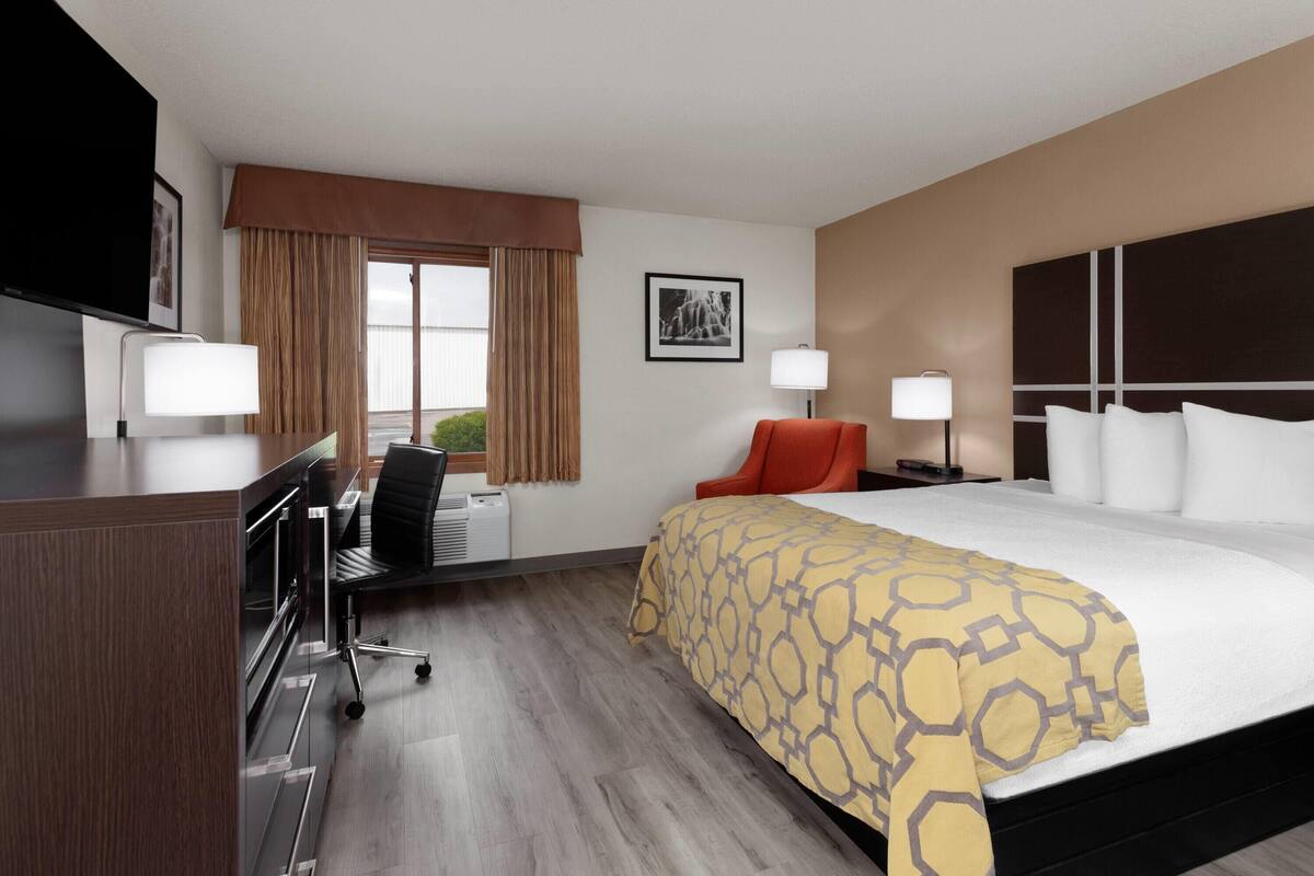 A hotel room with a large bed, a desk with a chair, a television, and a window with curtains.