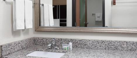 Un baño con encimera de granito, un espejo, un perchero para toallas y un pequeño envase de toallitas desmaquillantes Dove.
