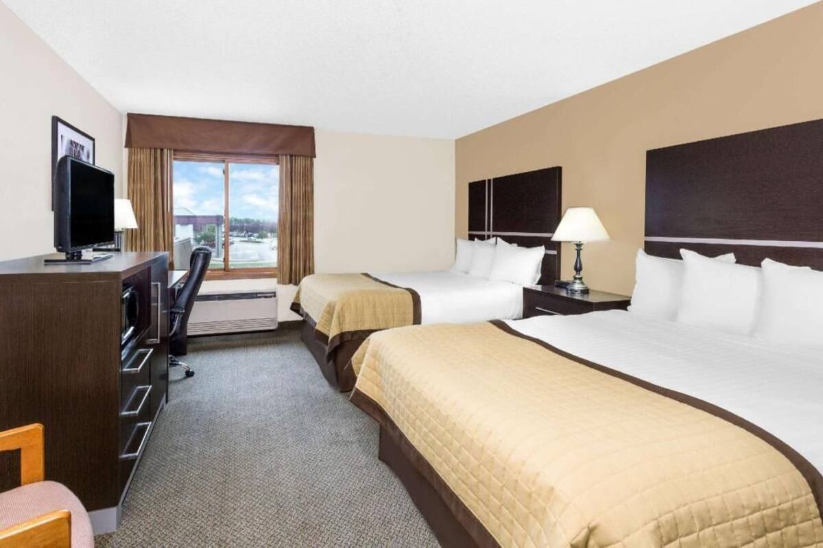 A hotel room with two beds, a desk with a TV, a chair, and a window with curtains.
