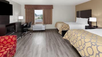 Una habitación de hotel con escritorio, dos camas, televisor y ventana con cortinas.