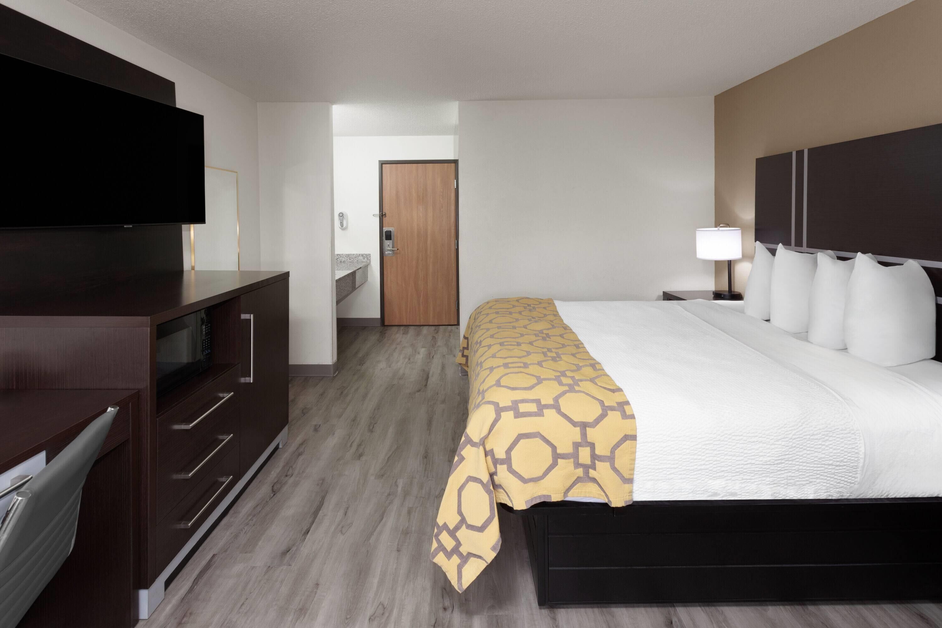 A hotel room with a bed, a TV, a desk, and a bathroom visible through an open door.