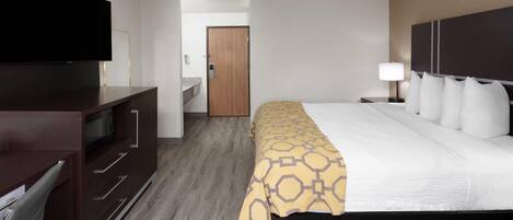 A hotel room with a bed, a TV, a desk, and a bathroom visible through an open door.