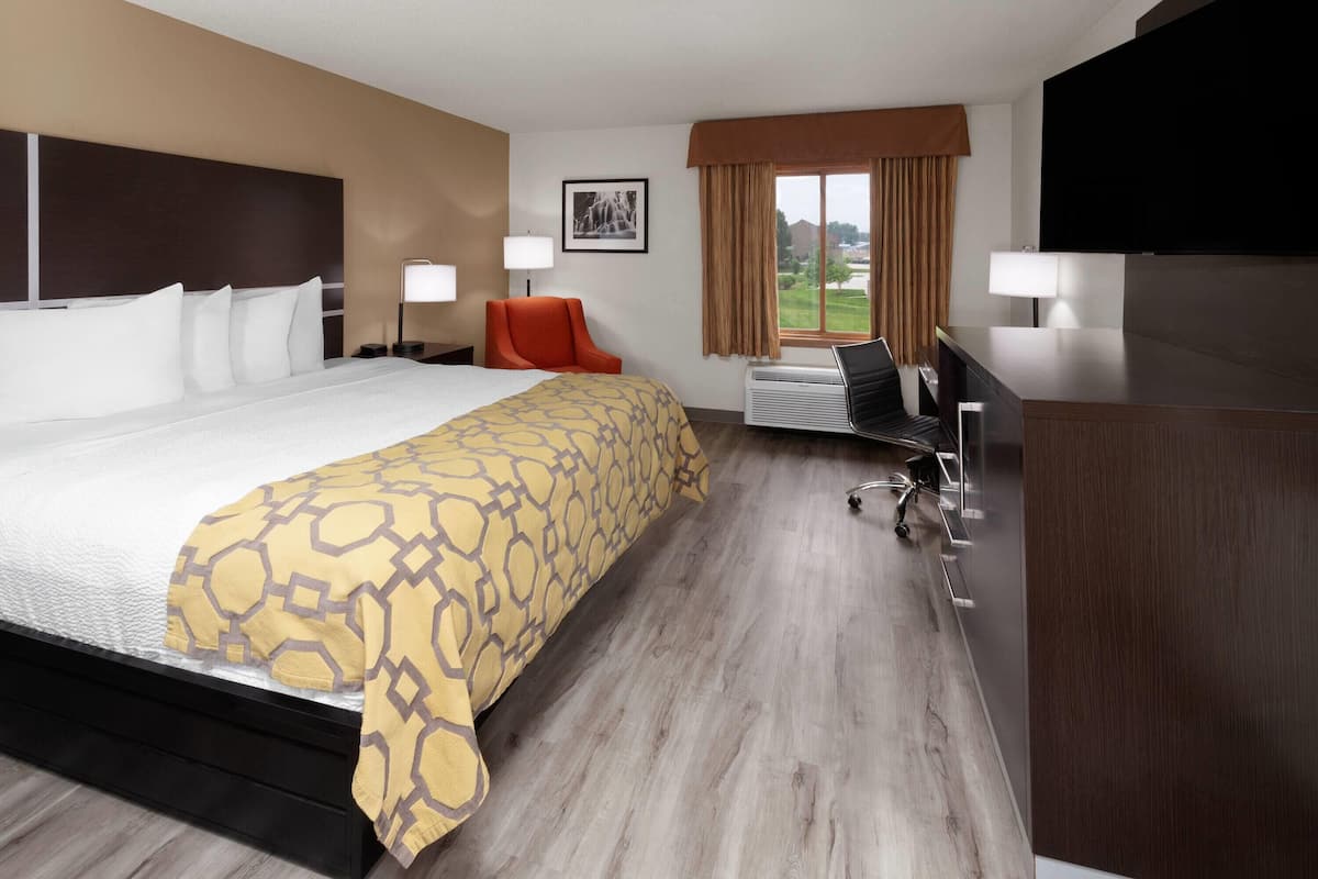 A hotel room with a large bed, a desk with a chair, a television, and a window with curtains.