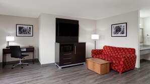 A modern hotel room with a wooden desk, a red patterned sofa, a flat-screen TV, and a small wooden side table. - Baymont by Wyndham Green Bay (Green Bay)