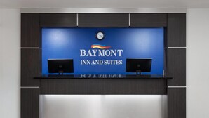 A reception desk with a blue backdrop displaying the Baymont Inn and Suites logo, two computer monitors, and a clock above. - Baymont by Wyndham Green Bay (Green Bay)
