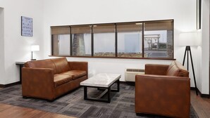 A modern room with two brown leather sofas, a marble coffee table, and a large window with blinds. - Baymont by Wyndham Green Bay (Green Bay)