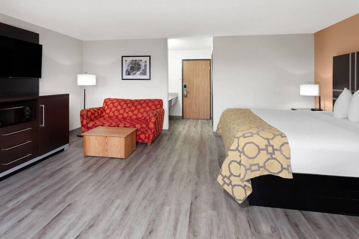 A hotel room with a bed, a sofa, a TV, a desk, and a door.