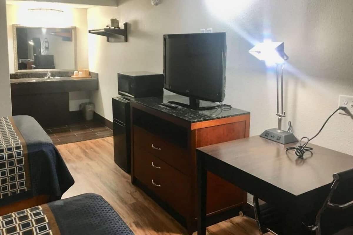 A hotel room with a bed, a desk, a television, and a desk lamp.