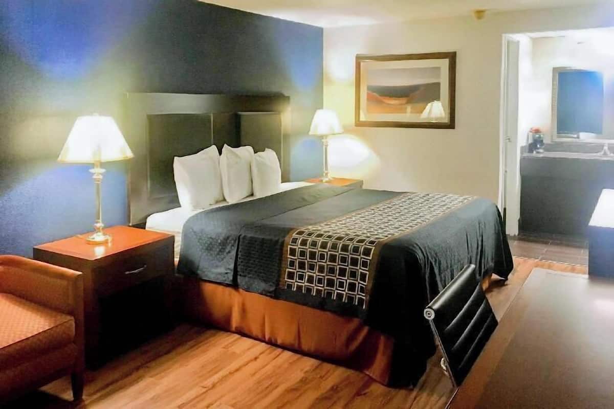 A hotel room with a bed, two bedside tables with lamps, a chair, a painting on the wall, and a mirror.