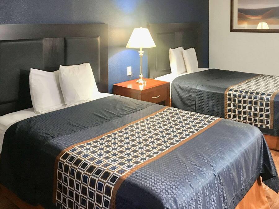 Ein Hotelzimmer mit zwei Betten, einem Nachttisch, einer Lampe und einem gerahmten Bild an der Wand.