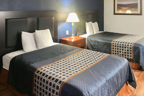 A hotel room with two beds, a nightstand, a lamp, and a framed picture on the wall.