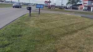 Un área verde con una calle, semáforos y edificios comerciales, incluyendo un restaurante Roosters.