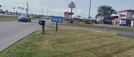 Un área verde con una calle, semáforos y edificios comerciales, incluyendo un restaurante Roosters.