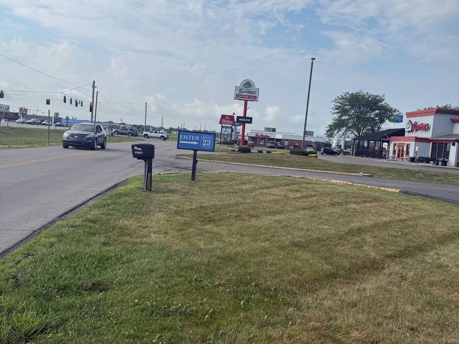 A grassy area with a road, traffic lights, and commercial buildings including a Roosters restaurant.