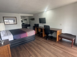 Quarto de hotel com cama, escrivaninha, cadeira e televisão.