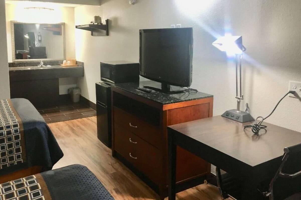 A hotel room with a bed, a desk, a television, and a desk lamp.