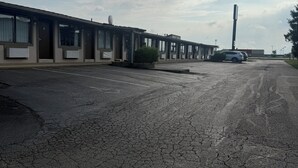 Una hilera de edificios de una planta con amplios ventanales, un estacionamiento con varios coches y un cielo despejado con nubes.
