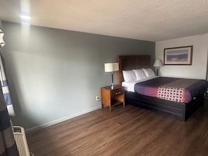 A hotel room with a bed, bedside table, lamp, and a painting on the wall.