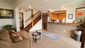 Eine Hotelhalle mit einer Rezeption, einer Treppe, einer Sitzecke mit einer Couch und einem kleinen Tisch mit Zeitschriften und einer Pflanze.