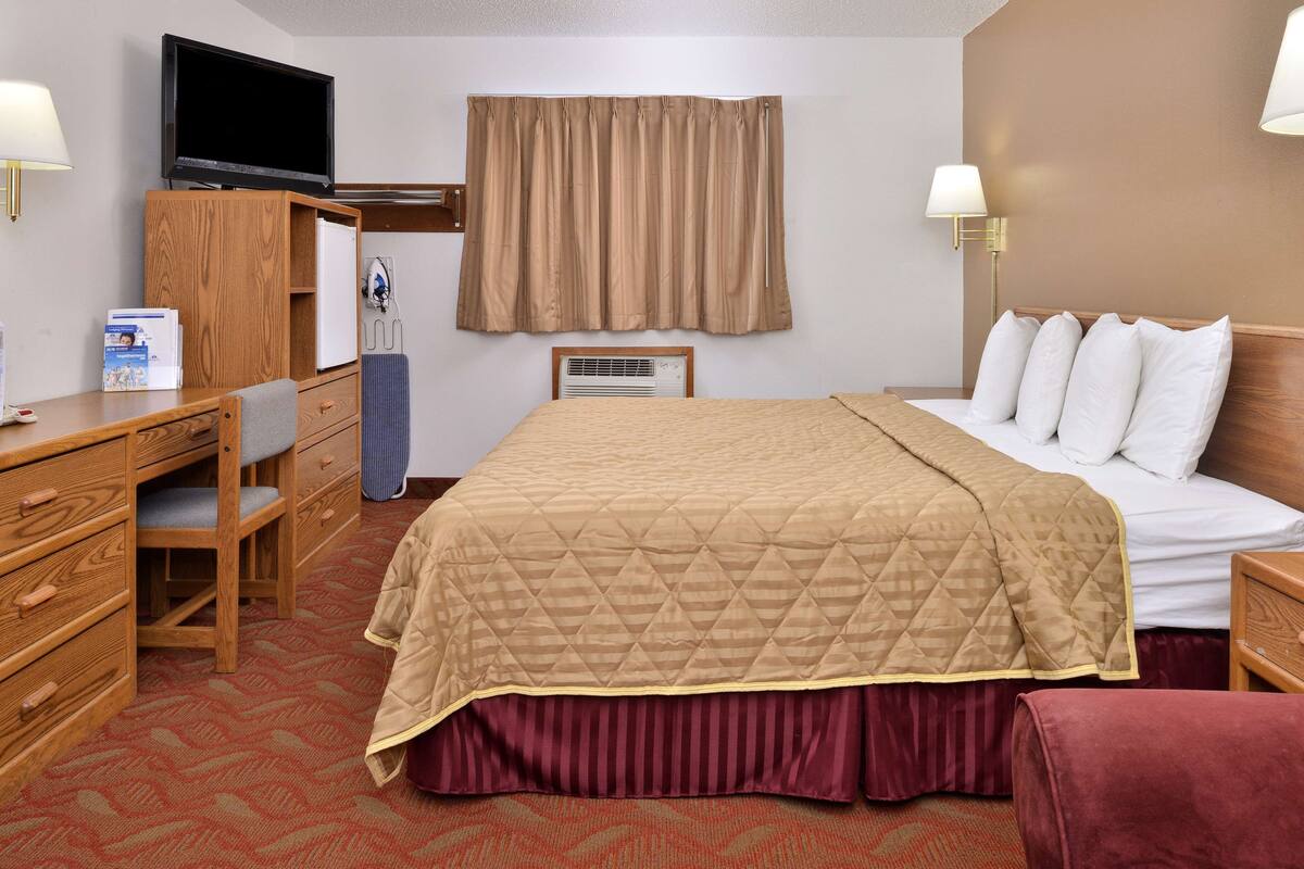 A hotel room with a bed, a desk, a chair, a television, and a window with curtains.