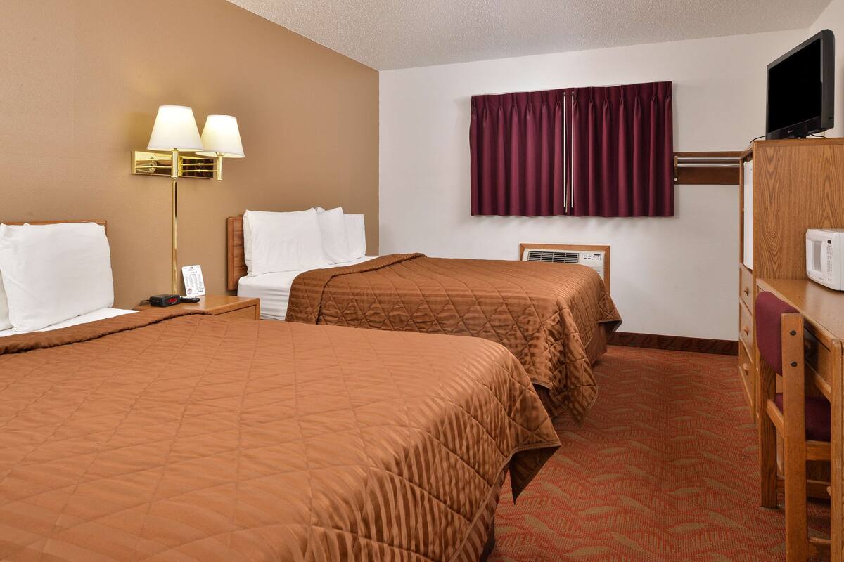 A hotel room with two beds, a TV, a desk with a computer, and a window with curtains.