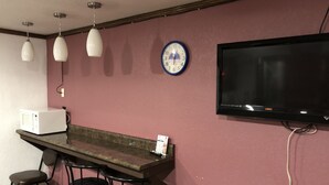 Eine Bar mit einer Mikrowelle, Barhocker, Pendelleuchten, einer Uhr und einem Flachbildfernseher.