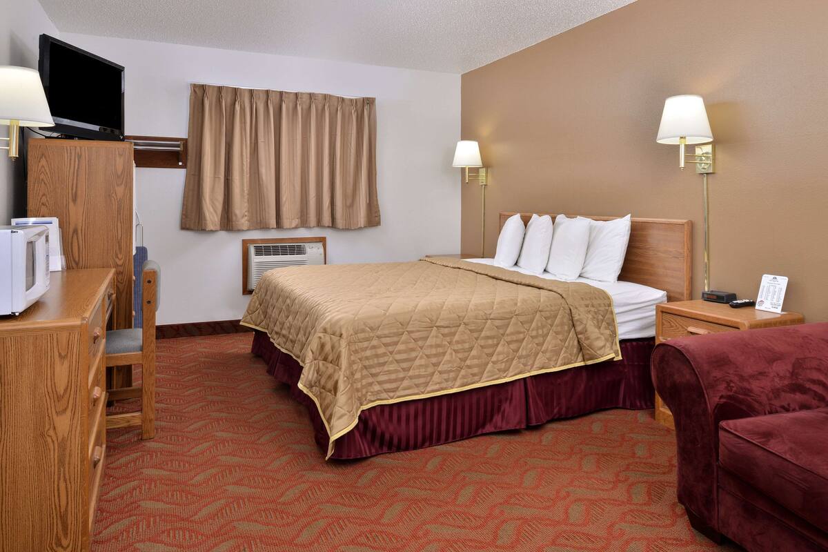 A hotel room with a bed, two bedside lamps, a TV, a desk, and a chair.