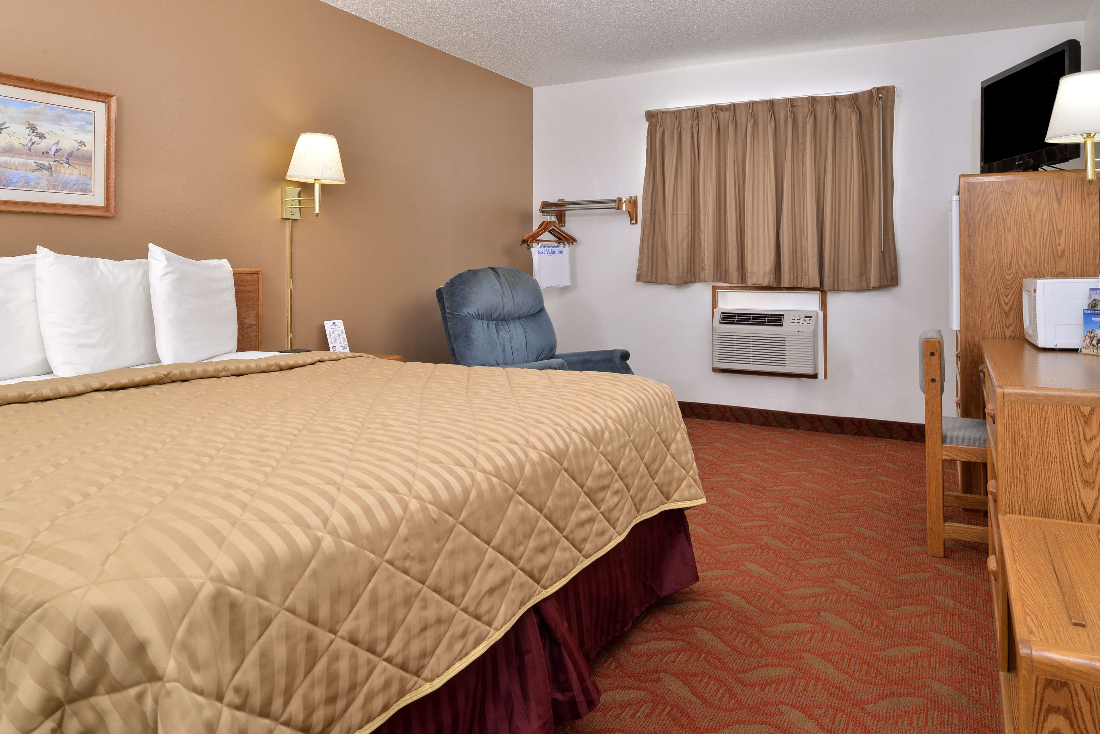 A hotel room with a large bed, a desk, a chair, a television, and an air conditioning unit.
