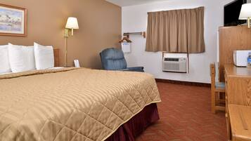 A hotel room with a large bed, a desk, a chair, a television, and an air conditioning unit.