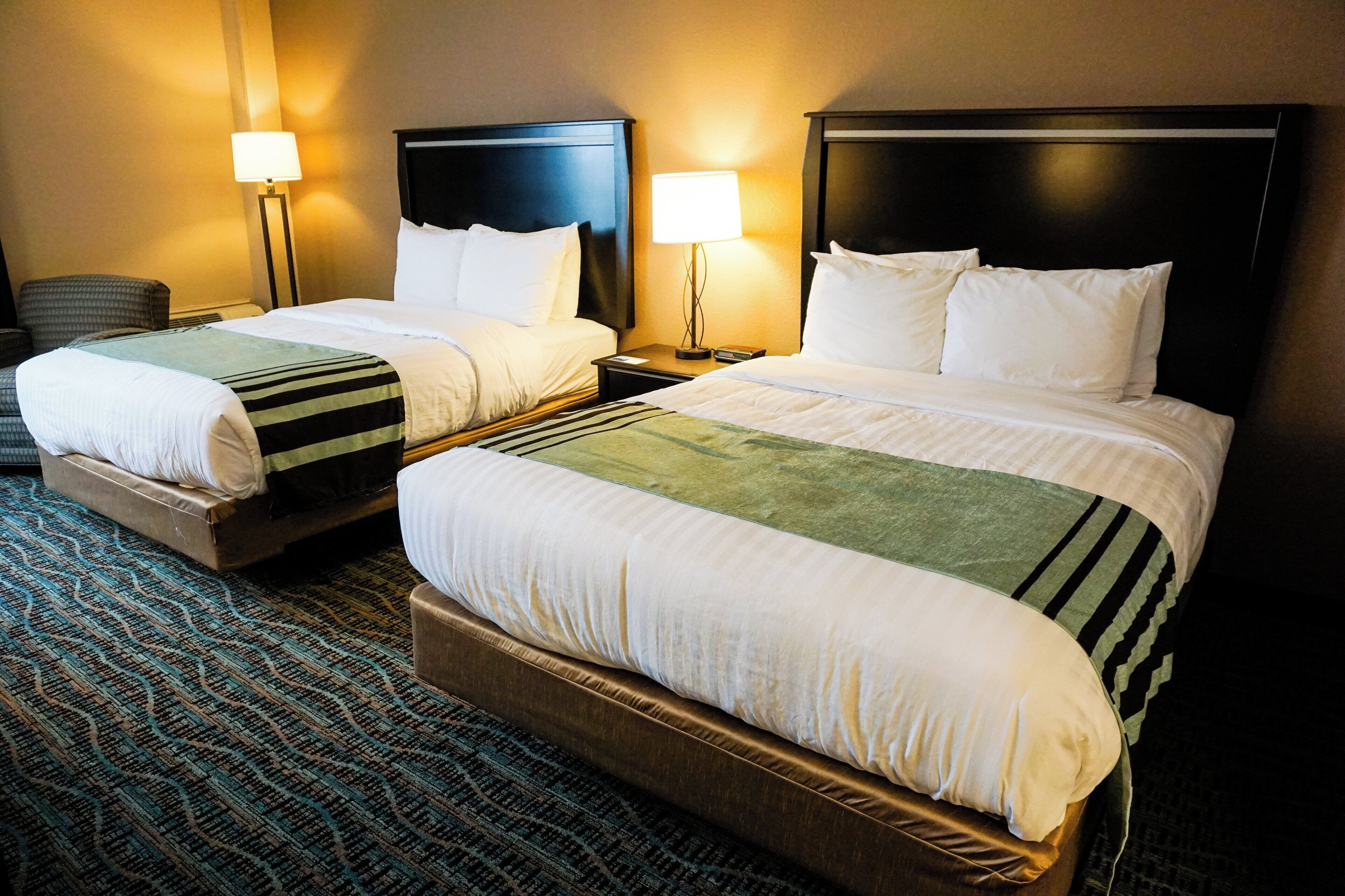 Une chambre d’hôtel avec deux lits, chacun doté d’une tête de lit, d’une table de chevet et d’une lampe. La chambre est recouverte d’un tapis à motifs.