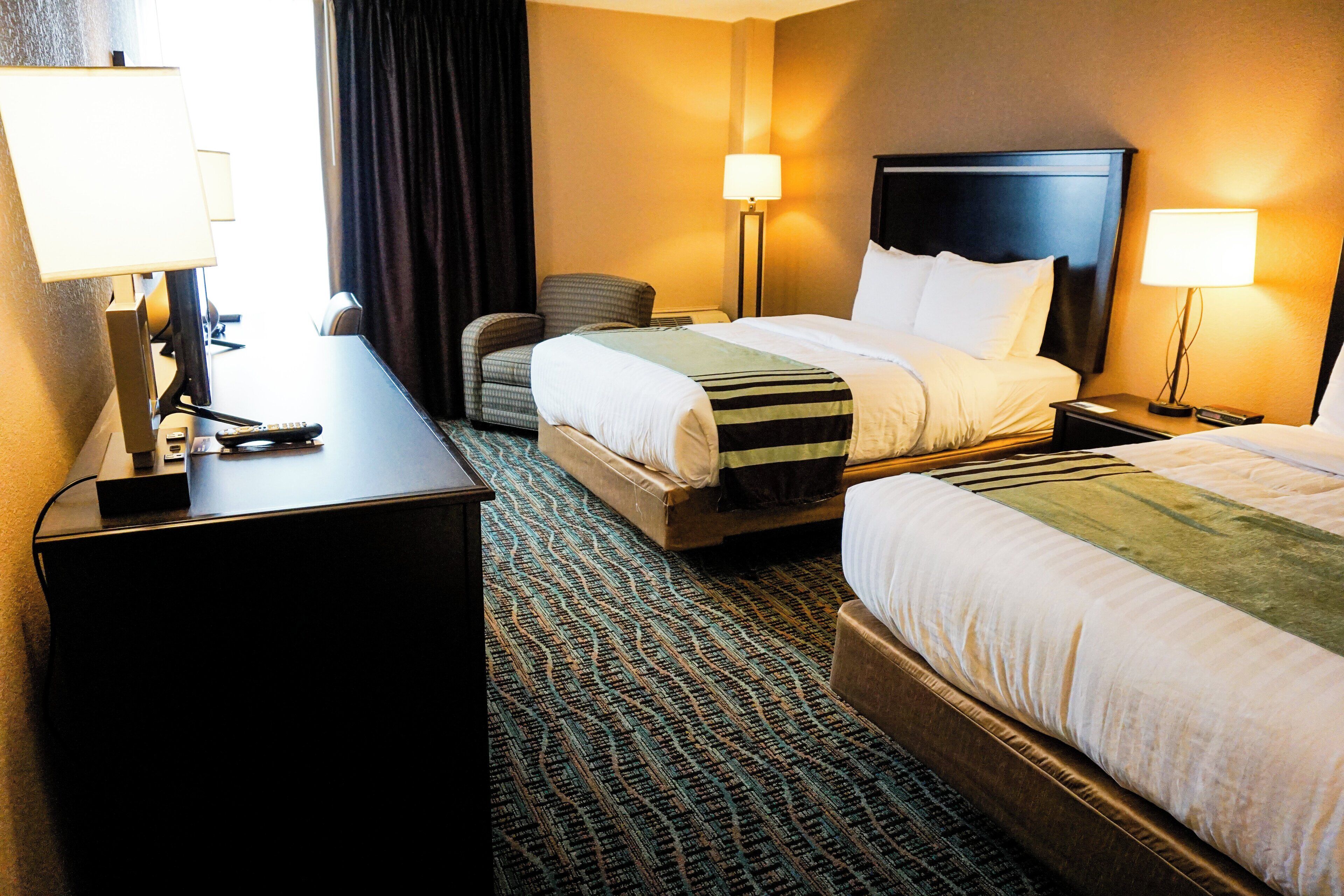 A hotel room with two beds, a desk, a chair, and two bedside lamps.