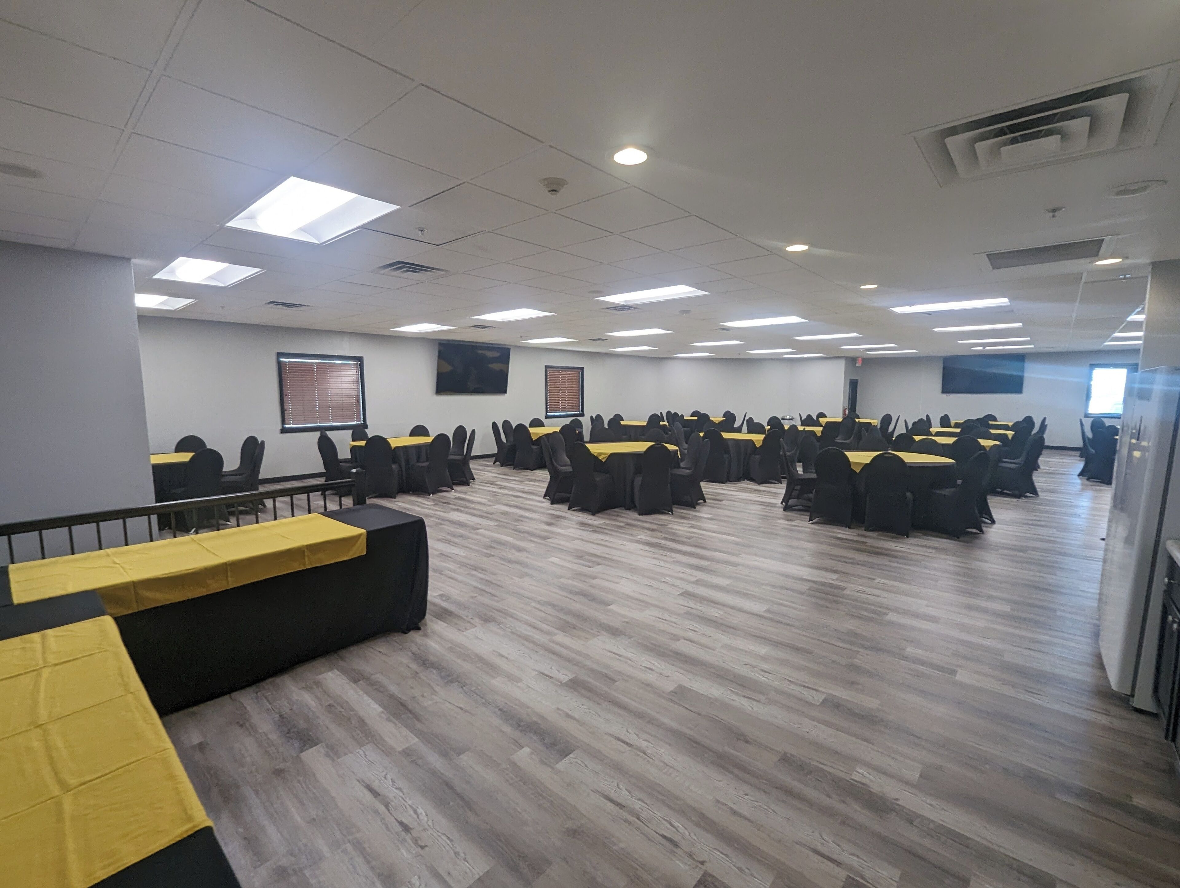 A conference room with multiple tables and chairs, equipped with ceiling lights and windows.