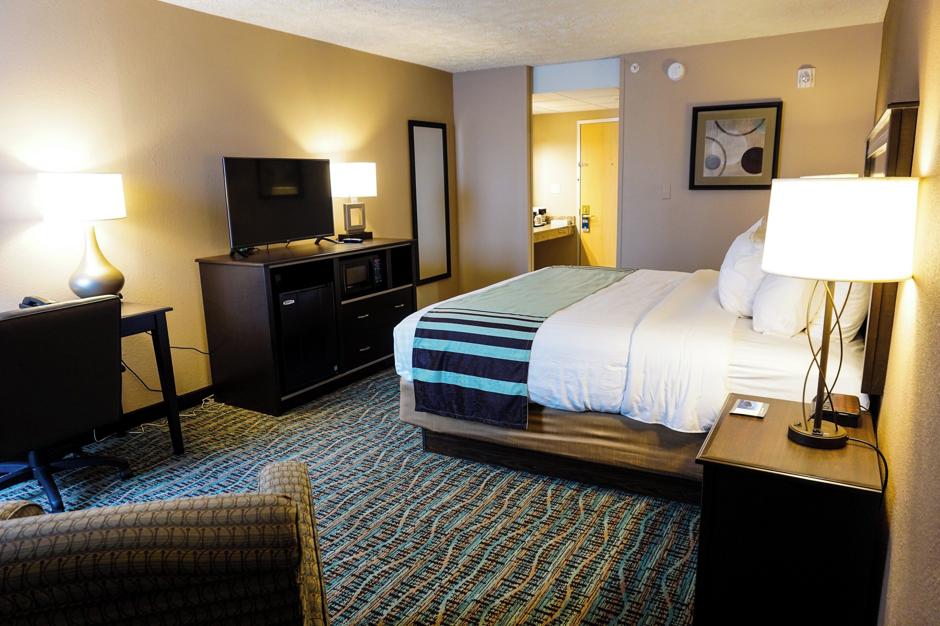 A hotel room with a bed, a desk with a computer, a TV, and a lamp.
