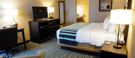 A hotel room with a bed, a desk with a computer, a TV, and a lamp.