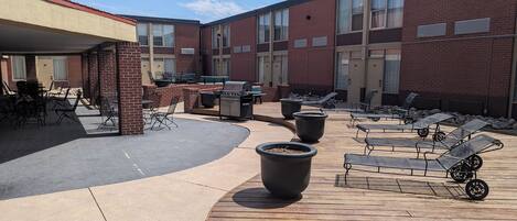 Un patio con mobiliario exterior, una parrilla y tumbonas.