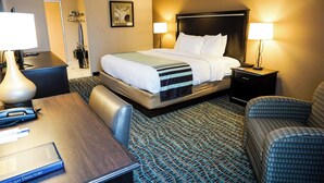 A hotel room with a bed, two bedside tables, a desk, a chair, and a guest directory.