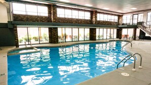 An indoor swimming pool with clear water, metal ladders, and large windows allowing natural light.