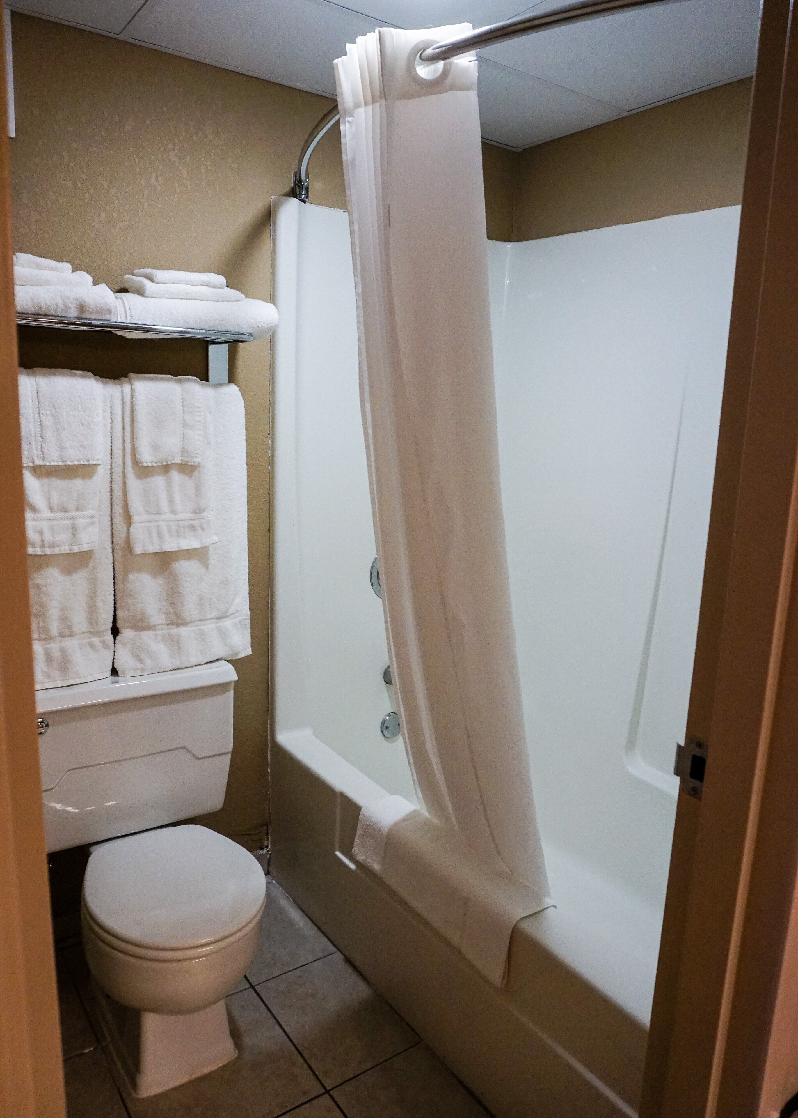 A bathroom with a toilet, a shower with a curtain, and a towel rack with folded towels.