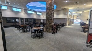 A spacious indoor area with multiple tables and chairs, a large stone pillar, and a ceiling with a sky-like design.