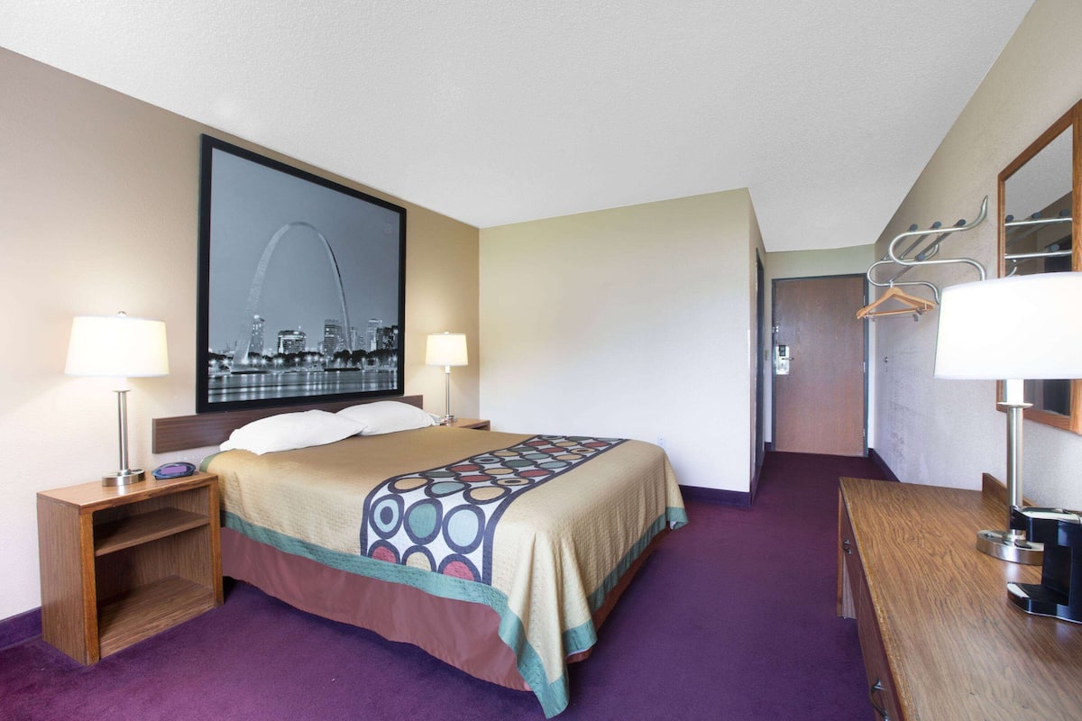 A hotel room with a bed, two bedside lamps, a wooden nightstand, a dresser, and a mirror.