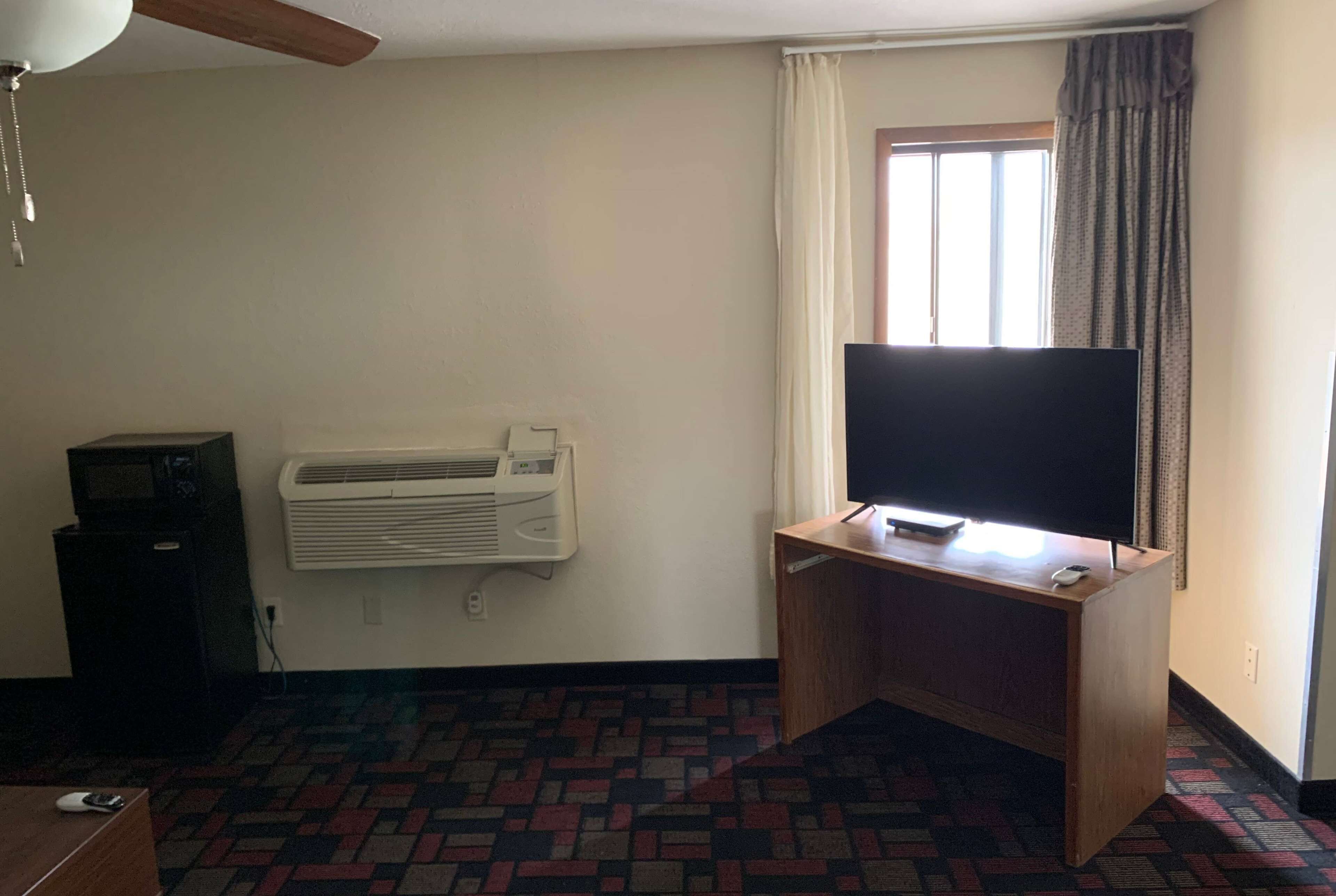 Una habitación con una televisión de pantalla plana sobre un escritorio de madera, un aire acondicionado montado en la pared y una alfombra estampada.