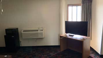 Una habitación con una televisión de pantalla plana sobre un escritorio de madera, un aire acondicionado montado en la pared y una alfombra estampada.