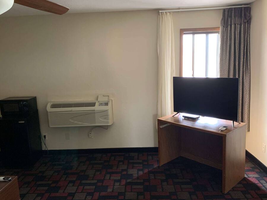 Una habitación con una televisión de pantalla plana sobre un escritorio de madera, un aire acondicionado montado en la pared y una alfombra estampada.