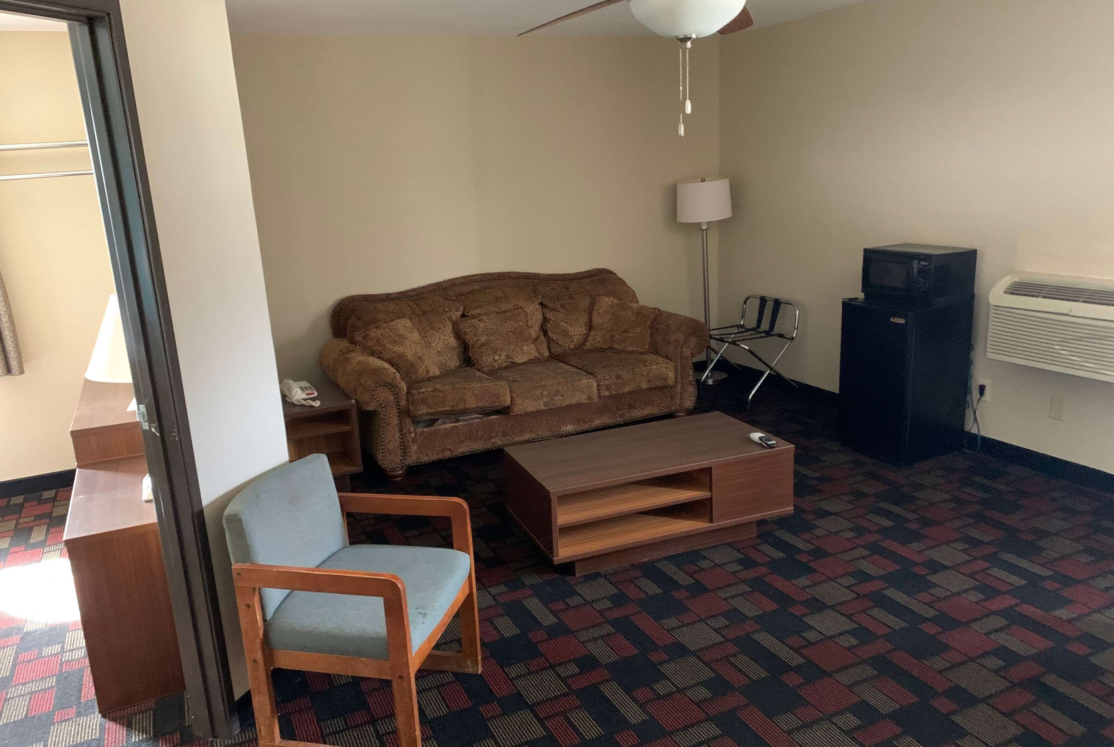 Una sala de estar con sofá, sillón, mesa de centro, lámpara, televisor y calefactor.