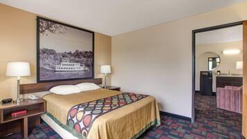 Hotelkamer met een bed, twee bedlampen, een nachtkastje, een lijst met een afbeelding aan de muur, een badkamer zichtbaar door een geopende deur en een kamerbreed tapijt met dessin.